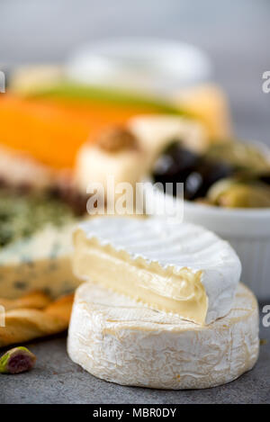 Assortiment de disque, semi-mous et les fromages aux olives, pains bâtons grissini, câpres, Raisin, sur fond de béton gris. Vue de dessus, copiez l'espace, mise à plat. Sélection de fromages apéritif assiette. Banque D'Images