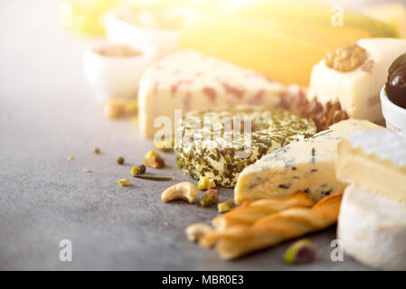 Assortiment de disque, semi-mous et les fromages aux olives, pains bâtons grissini, câpres, Raisin, sur fond de béton gris. Vue de dessus, copiez l'espace, mise à plat. Sélection de fromages apéritif assiette. Banque D'Images