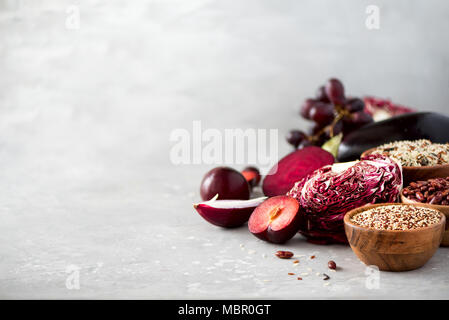 Concept de l'alimentation propre. Les légumes crus purple sur fond de béton gris. Violet aubergine, betterave, chou-fleur, haricots violets, prunes, raisins, oignon, le quinoa, le riz. Ingrédients pour la cuisson, copy space Banque D'Images