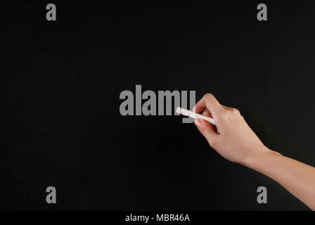 Woman hand holding craie blanche en face de l'école vide tableau noir Banque D'Images