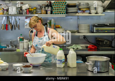 Femme verse du lait dans un bol alors que la cuisson dans une cuisine commerciale dans un café en Irlande. Banque D'Images