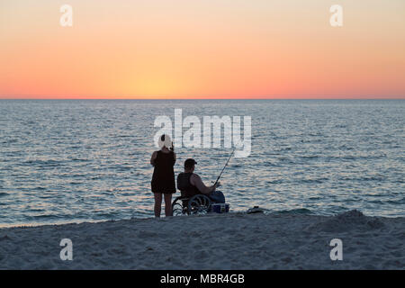 Couple sur la plage au coucher du soleil. L'homme en fauteuil roulant, la pêche. Banque D'Images