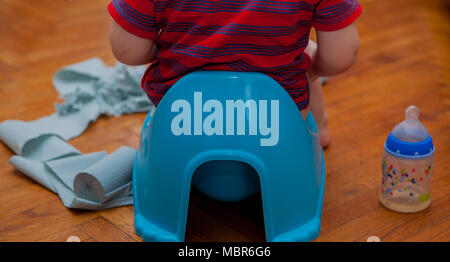 Little baby sitting sur pot de chambre avec du papier toilette et suce sur un fond brun. Banque D'Images