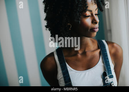 Pretty young african american woman posing in jeans pantalons par le mur dans la chambre Banque D'Images