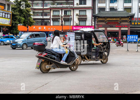 Une jeune femme et enfant billet sur un scooter. L'enfant est assis en face de la femme et est titulaire d'une feuille dans sa main. Yangshuo, Chine. Banque D'Images