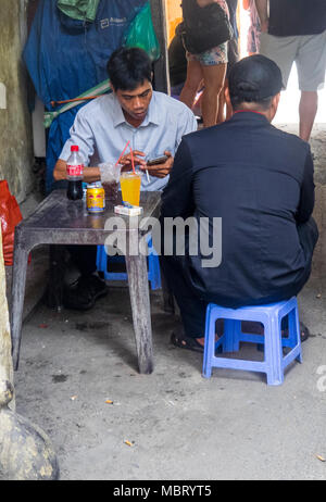 Deux hommes assis sur des tabourets en plastique sur le trottoir d'avoir des boissons fraîches, Ho Chi Minh City, Vietnam. Banque D'Images