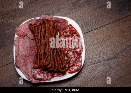 Saucisses différentes de tranchage sur une plaque blanche Banque D'Images