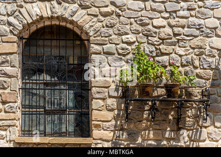 Vieux Mur de pierre avec fenêtre, vitraux, durée et pots qui ont des usines à fleurs roses Banque D'Images