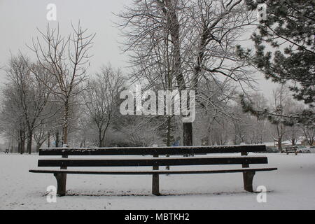 Un banc typique dans le parc juste après la chute de neige dans un jour nuageux. Banque D'Images