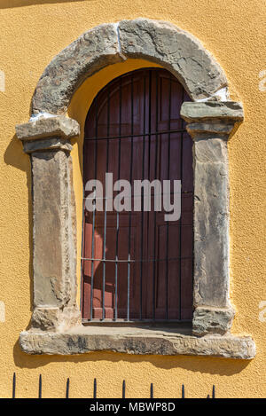 Fenêtre avec arch avec châssis en pierre et clôture sur mur jaune Banque D'Images