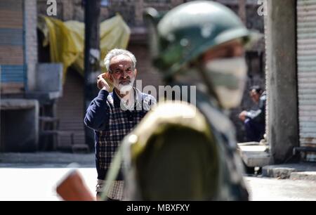 12 avril 2018 - Srinagar, J&K, Inde - un homme marche du Cachemire indien passé un trooper paramilitaires qui monte la garde pendant les restrictions dans Srinagar, Cachemire sous administration indienne. Comme les zones à majorité musulmane du Cachemire jeudi a observé un arrêt complet pour protester contre la mort de 4 civils dans les tirs de l'armée près du site de rencontre à Kulgam de district du Cachemire indien. Commerces, écoles et collèges ont été fermées à la suite d'un appel par les séparatistes, alors que les autorités couvre feu dans plusieurs domaines pour arrêter les manifestations de rue. Pendant ce temps, la pierre-qui tombe des incidents ont été signalés dans certaines parties de Srinagar Banque D'Images