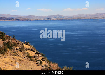 Tricoter un homme assis sur le bord de la falaise surplombant l'île de Taquile sur le lac Titicaca en direction de la bolivie Banque D'Images