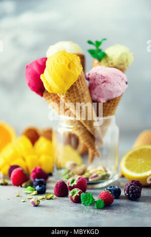 Boules de crème glacée coloré en cônes alvéolés avec différentes saveurs - mangue, citron vert, menthe, pistache, orange, fraises, framboises, bleuets. Concept d'été Banque D'Images