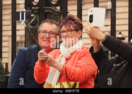 Un couple d'âge moyen, de sourire, de prendre une à l'extérieur de l'avant garde-corps selfies de Buckingham Palace avec une mains selfies prenant un autre Banque D'Images