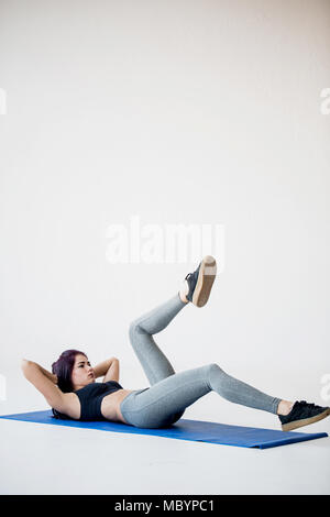 Jeune brunette sportive fait la location crunches allongé sur le tapis de yoga studio dans le livre blanc. Banque D'Images
