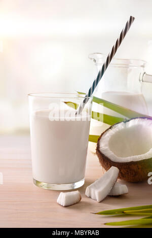 Le lait de coco dans le verre avec des fruits sur la table en bois blanc sur un arrière-plan de cuisine. Autre concept de lait. Vue de face. Composition verticale. Banque D'Images