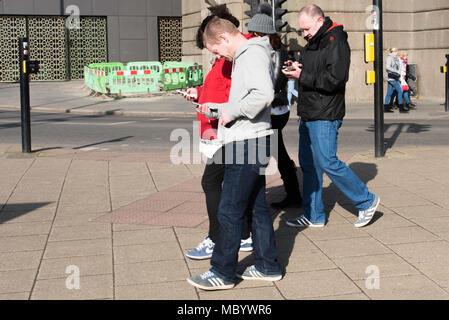 Un groupe de personnes à la recherche de leurs téléphones portables comme ils marchent le long des quais, à Newcastle upon Tyne et Wear, Angleterre. Banque D'Images