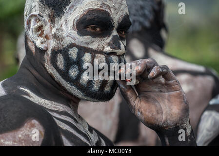 Un Masalai d'Omo avec squelette peinture sur visage de fumer la cigarette, le mont Hagen Spectacle culturel, Papouasie Nouvelle Guinée Banque D'Images