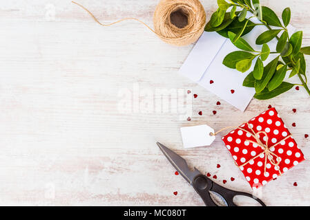 Carte vide lié en pointillés rouges sur la boîte-cadeau sur fond de bois blanc. Copier l'espace. Sequins en forme de coeur dispersés, une enveloppe et des matériaux d'emballage. Banque D'Images