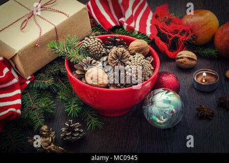 Décoration de Noël - rouge bol plein de cônes de sapin, boîte-cadeau enveloppé dans du papier kraft, des branches de pins, bougie, écrous, d'anis, pommes, des jouets de Noël et rouge Banque D'Images
