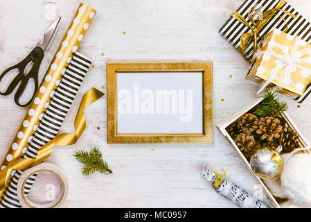 Cadre ptoto doré, des boîtes-cadeaux, une caisse pleine de pommes de pin et des jouets de Noël et des matériaux d'emballage en bois blanc sur un vieux fond. Concept de Noël Banque D'Images