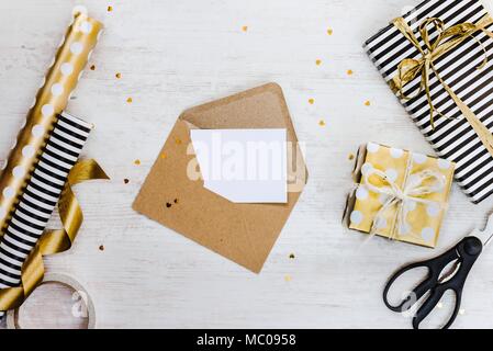 Carte de voeux vierge dans une enveloppe craft, coffrets cadeaux et matériaux d'emballage en bois blanc sur un arrière-plan. Banque D'Images