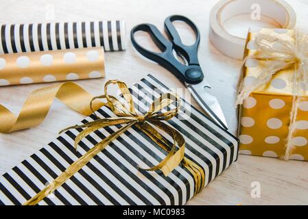 Close up de coffrets cadeaux enveloppés en noir et blanc à rayures et parsemé d'or et les matériaux d'emballage en papier blanc sur un fond vieux bois. Banque D'Images