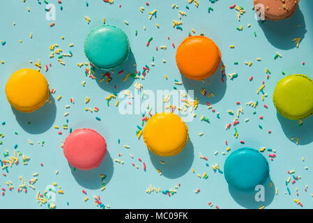 Vue de dessus de macarons colorés dispersés et saupoudre de sucre sur fond bleu. Résumé Contexte de l'alimentation. Banque D'Images
