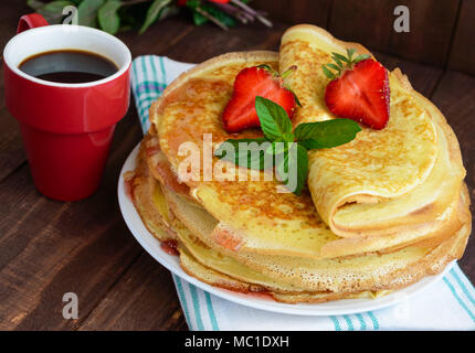 Pile de crêpes dorées avec des fraises et de la confiture de fraise, décoratives feuille de menthe. Close-up Banque D'Images