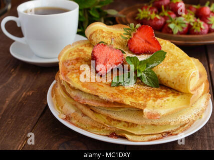 Pile de crêpes dorées avec des fraises et de la confiture de fraise, des feuille de menthe et une tasse de thé. Close-up Banque D'Images