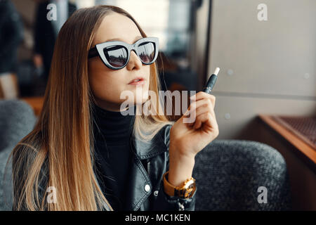 Jeune fille s'asseoir dans la fumée et lieu caffee cigarette électronique portent des lunettes Banque D'Images