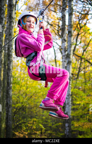 Jeune fille sur la tyrolienne entre les arbres dans un parc d'aventure. Banque D'Images