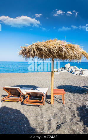 L'île de Paros, Cyclades, en Grèce. Des parasols de paille et des chaises longues sur la plage dorée. Banque D'Images