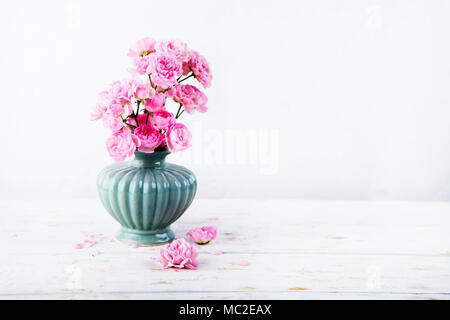 Sweet pink roses fleurs dans des vases sur fond de bois peint en blanc contre mur blanc. Focus sélectif. Place pour le texte. Image tonique Banque D'Images