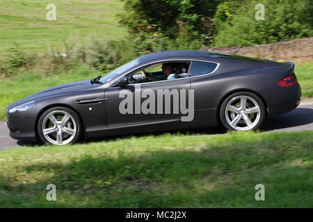 Noir mat Aston Martin DB9 dans le profil (vue latérale) conduite rapide sur une route de campagne. Banque D'Images