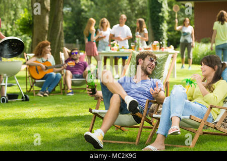 Les amis s'asseoir sur les chaises longues et boire des boissons et un barbecue dans le jardin avec des amis Banque D'Images