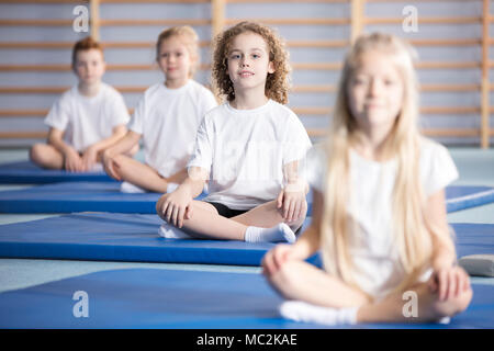 Smiling boy et ses amis assis sur un tapis bleu au cours de gymnastique corrective Banque D'Images