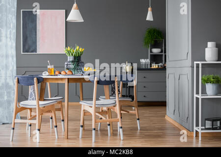 Sol en bois, peinture-feux de chaises autour d'une petite table à manger avec des pâtisseries et un tableau abstrait sur un mur gris d'une salle à manger avec des plantes d'intérieur Banque D'Images