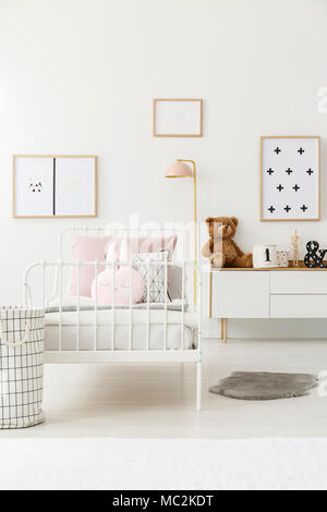 Blanc, metal kids lit avec oreiller lapin debout dans cette chambre lumineuse à l'intérieur de simples affiches sur le mur Banque D'Images