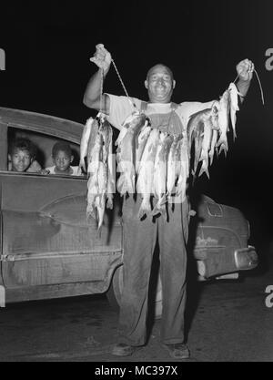 Père affiche fièrement un Stringer, de poisson-chat pendant que les enfants d'attendre dans la transmission Dynaflow automobile Buick, ca. 1963. Banque D'Images