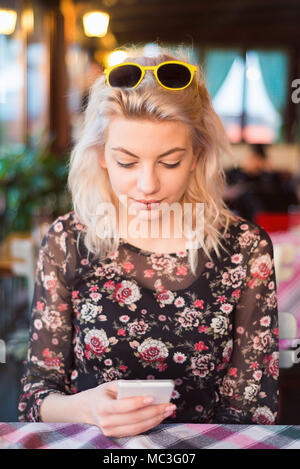 Belle jeune femme looking at mobile phone in restaurant Banque D'Images