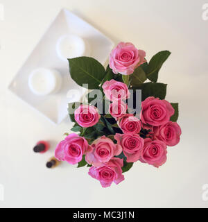 Un bouquet de fleurs roses dans un vase. La photo est prise d'en haut (flatlay). En plus il y a de roses bougies blanches et deux ongles. Banque D'Images