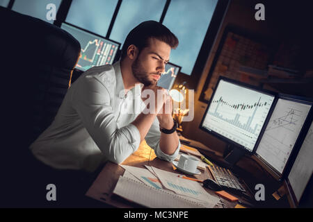 L'accent des commerçant ou investisseur sérieux travail de nuit les heures supplémentaires l'analyse de stock trading graphiques à des moniteurs d'ordinateur au marché contrôle Banque D'Images