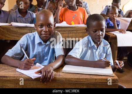 L'Ouganda. 13 juin 2017. Les enfants ougandais souriant assis à un bureau dans une salle de classe de l'école primaire de Kayanja. Banque D'Images