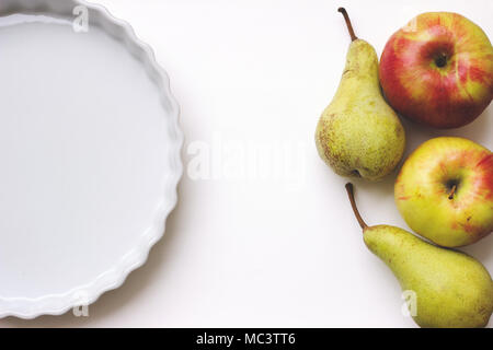 Céramique blanche vide tart ou circulaire allant au four, sur le tableau blanc, avec des pommes et des poires ; with copy space Banque D'Images