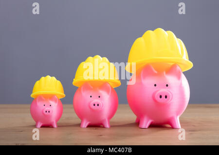 Close-up de l'augmentation de Pink Piggy Banks avec casque jaune bureau en bois Banque D'Images