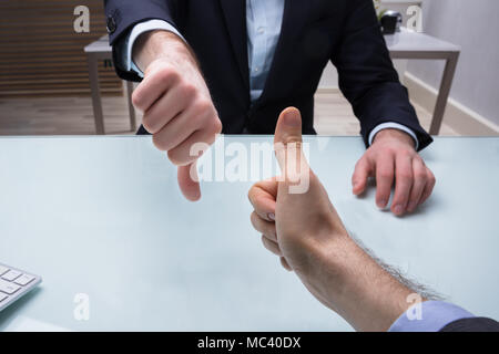 Businessman Showing Thumb Up et le pouce vers le bas sur Desk In Office Banque D'Images