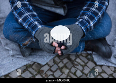 La main de mendiant portant des gants Holding Disposable Cup Banque D'Images