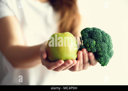 Femme en blanc T-shirt holding geen apple et le brocoli dans ses mains. Copier l'espace. Nettoyer detox, Manger végétarien, végétalien, concept brut Banque D'Images