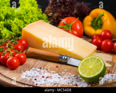 Planche de bois avec fromage parmesan, tomates cerises fraîches, de la laitue, sel de mer, de lime et le poivron rouge. Le couteau pour couper les légumes. L'appétissant Banque D'Images